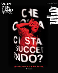 Locandina di Wonderland Festival 2026: una performer illuminata di rosso davanti alla domanda “Che cosa ci sta succedendo?”. Dal 6 al 29 novembre 2026 a Brescia.